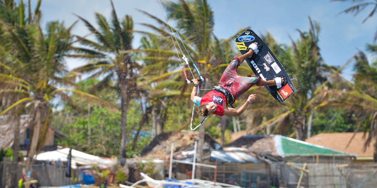 Kitesurfer beim Tricksen vor dem palmengesäumten Strand