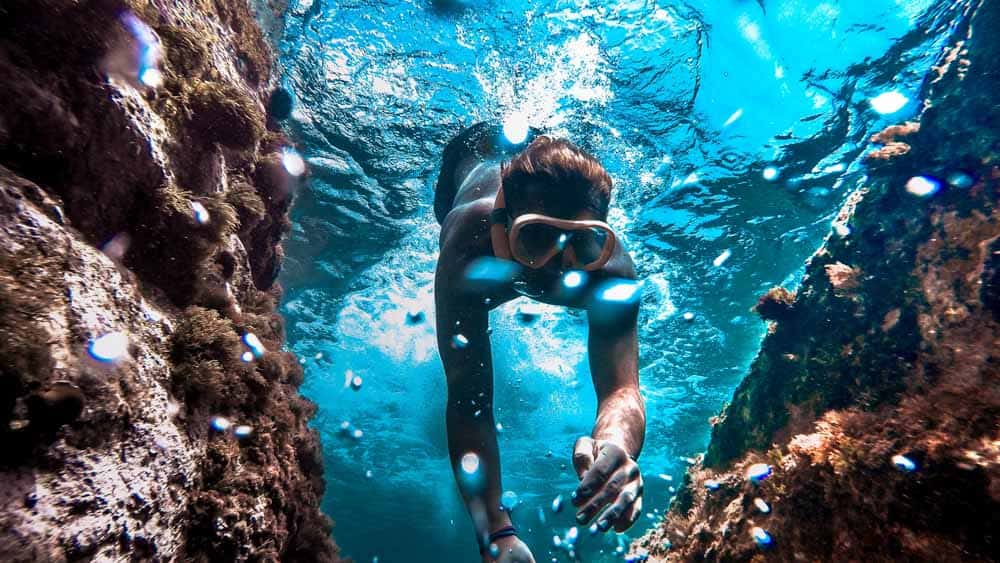 Unterwasseraufnahme einer Person, die mit einer Schnorchelmaske in türkisfarbenes Wasser eintaucht