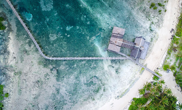 Luchtopname van Cloud 9 surfspot in Siargao, Filippijnen. Aqua blauw water omringt een kleine steiger en een gebouw op de oevers van het witte zandstrand