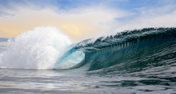 Nahaufnahme einer brechenden Welle mit einem sanften Sonnenuntergangshimmel im Hintergrund. Diese Welle wurde in Siargao aufgenommen, der Surfhauptstadt der Philippinen.