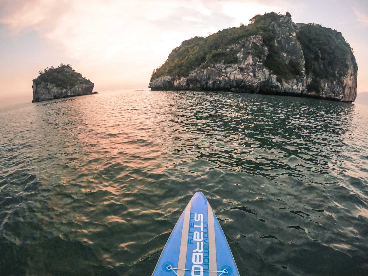 stand up paddle boarding bij zonsopgang. een roze zon werpt reflecties over het water waar twee kleine eilandjes liggen. gefotografeerd in sam roi yot nationaal park in Thailand