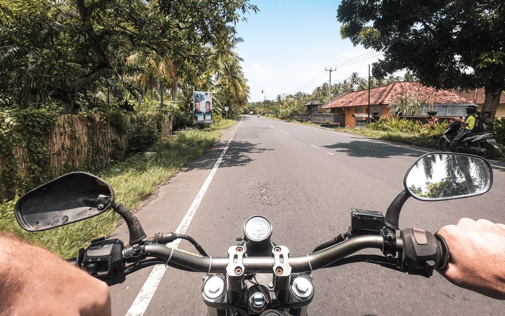 View of motorcycle handlebars while driving down the road during Bali road trip