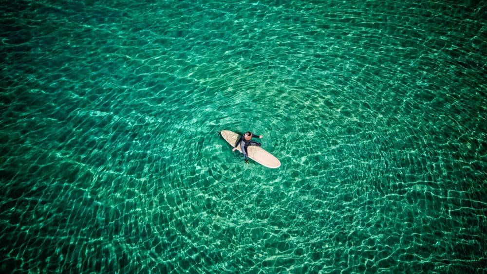 Beautiful surf photography of man sitting on surfboard in clear green water