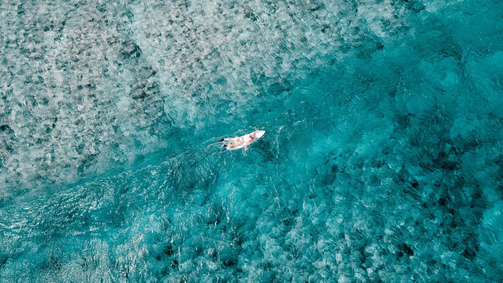 Photo prise par un drone d'un surfeur pagayant dans une eau bleue et limpide aux Maldives.