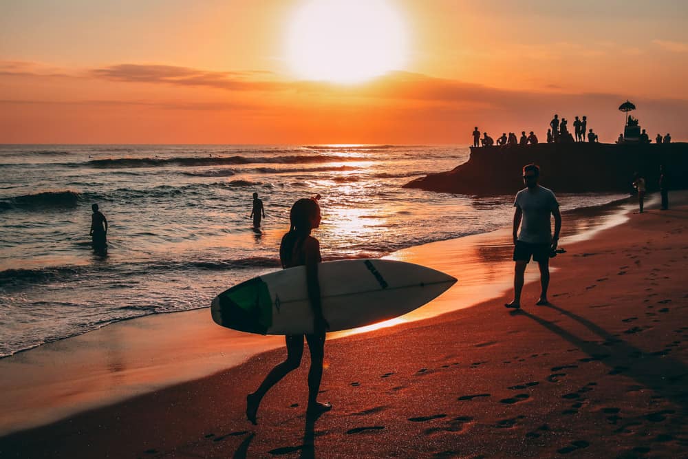 Atemberaubender Sonnenuntergang mit einem Surfer, der ein Surfbrett über den Strand von Bali trägt