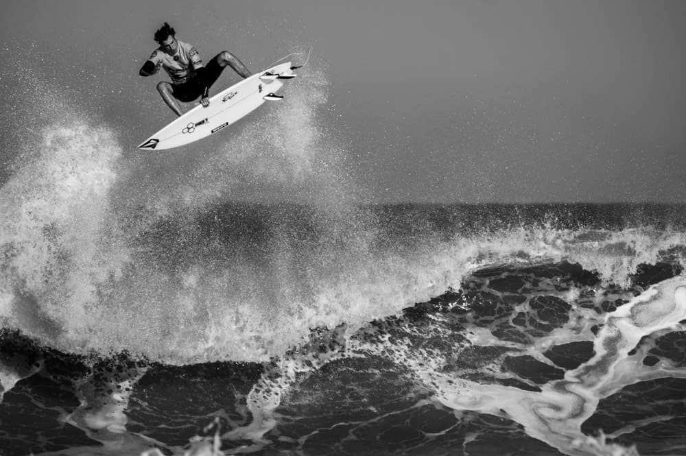 Schwarz-Weiß-Fotografie eines Surfers, der von der Spitze einer rauen Welle abspringt