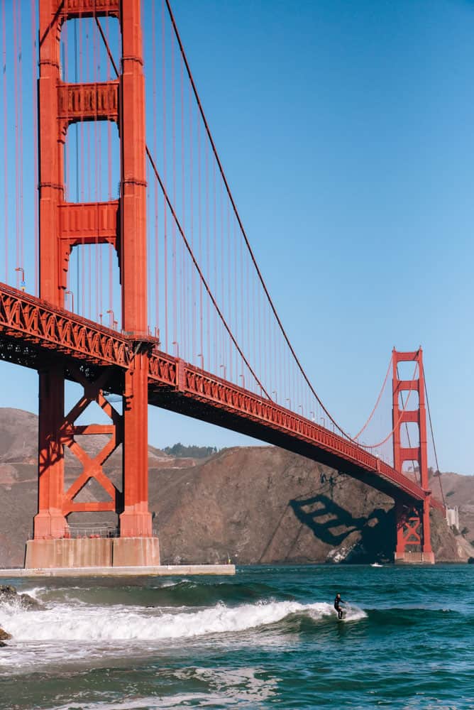 photographie de surf de san francisco ; un surfeur surfe sur une vague sous le pont du golden gate