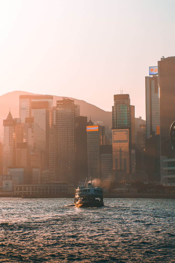 hongkong fähre nähert sich dem von wolkenkratzern gesäumten ufer bei sonnenuntergang