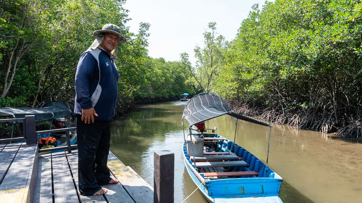 Petit bateau et chauffeur attendant sur les rives de la rivière Pranburi, entourée de mangroves.