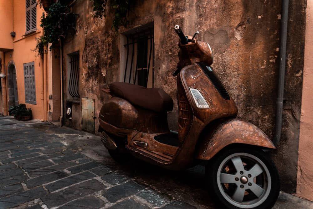 Rusty brown vespa parked in front of wall of same colour in Antibes Old Town