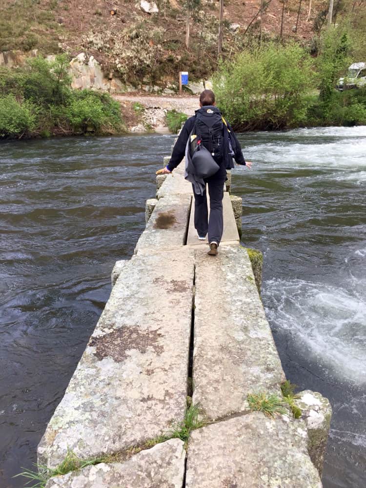 woman walking across narrow stone path in a river