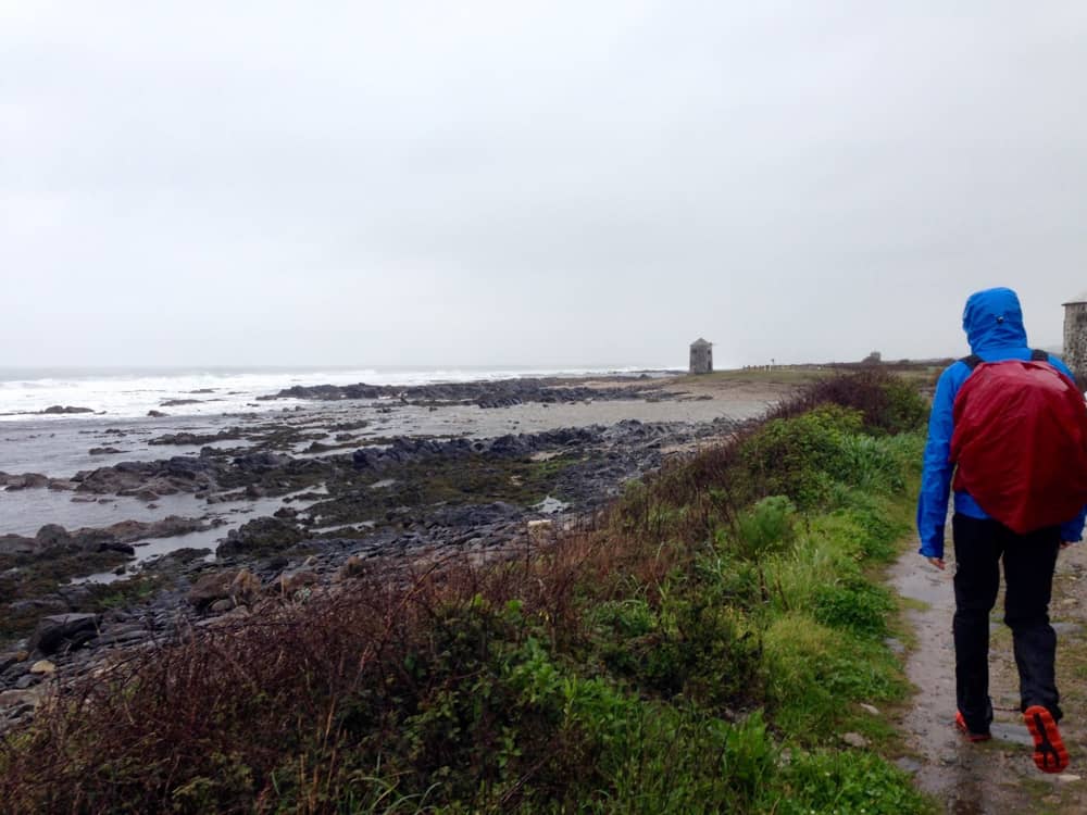 Mann mit aufgesetzter Kapuze beim Wandern auf dem portugiesischen Camino an einem regnerischen Tag