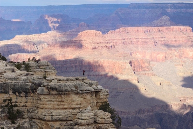 paysage ombragé du grand canyon avec une toute petite personne debout sur le bord d'une paroi rocheuse surplombant le paysage