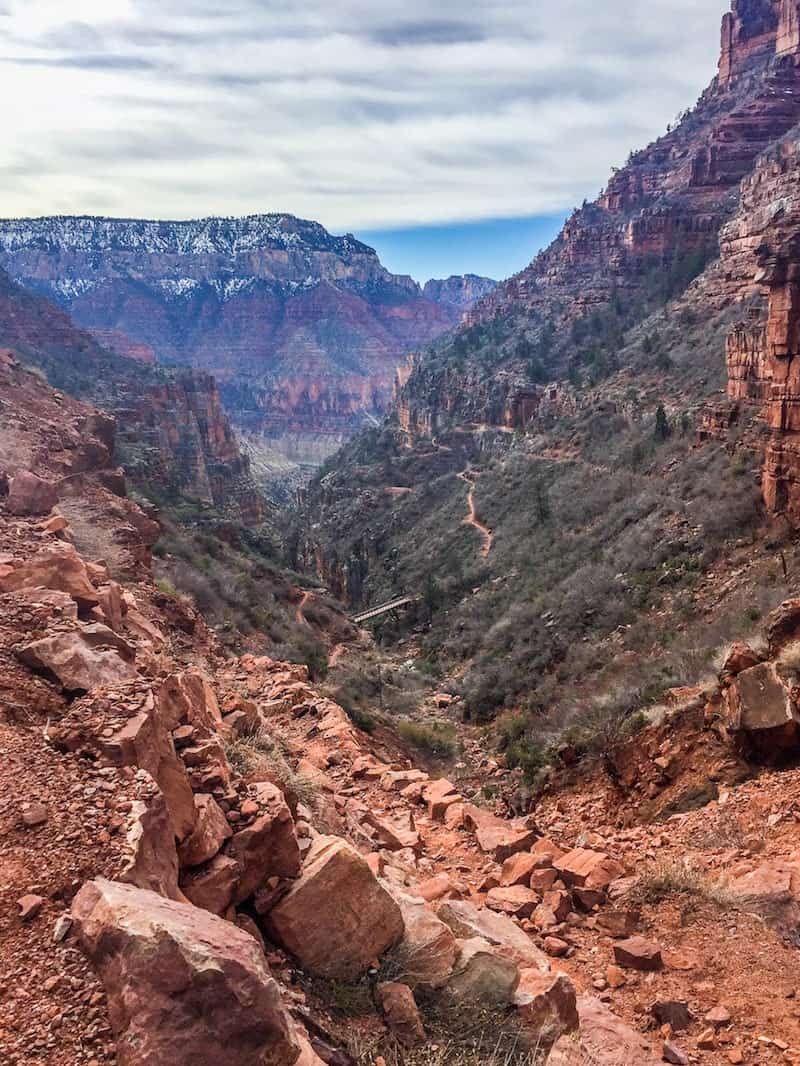 rote Felsen, die von den Klippen des Grand Canyon abbröckeln, mit dürren grünen Sträuchern, die auf den Hügeln im Hintergrund wachsen