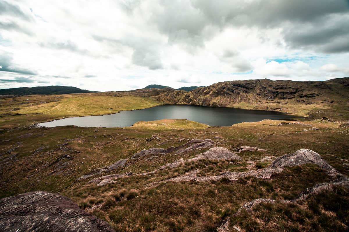 Paysage d'humeur à Barley Lake, West Cork. L'eau du lac est grise/noire et chatoyante dans la lumière douce, les nuages sont dans le ciel, l'herbe rugueuse entoure le paysage.