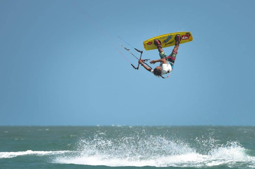 plusieurs fois champion d'asie de kitesurf, "yo" narapichit pudla, en kitesurf sur les eaux bleues de thailande. Il est en l'air, inversé, faisant une figure alors que l'eau éclabousse sous lui.