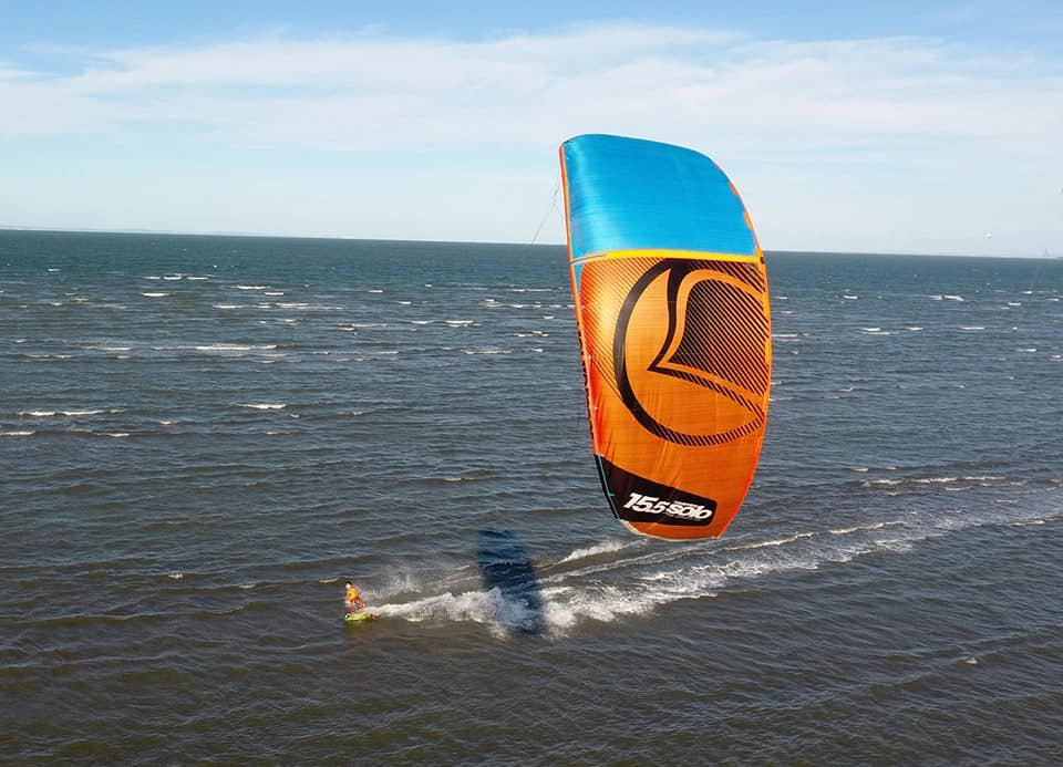 graues, kabbeliges Wasser in Queensland, Australien, mit einem Kitesurfer von rechts nach links, der einen 15 m langen orange-blauen Cabrinha-Drachen fliegt