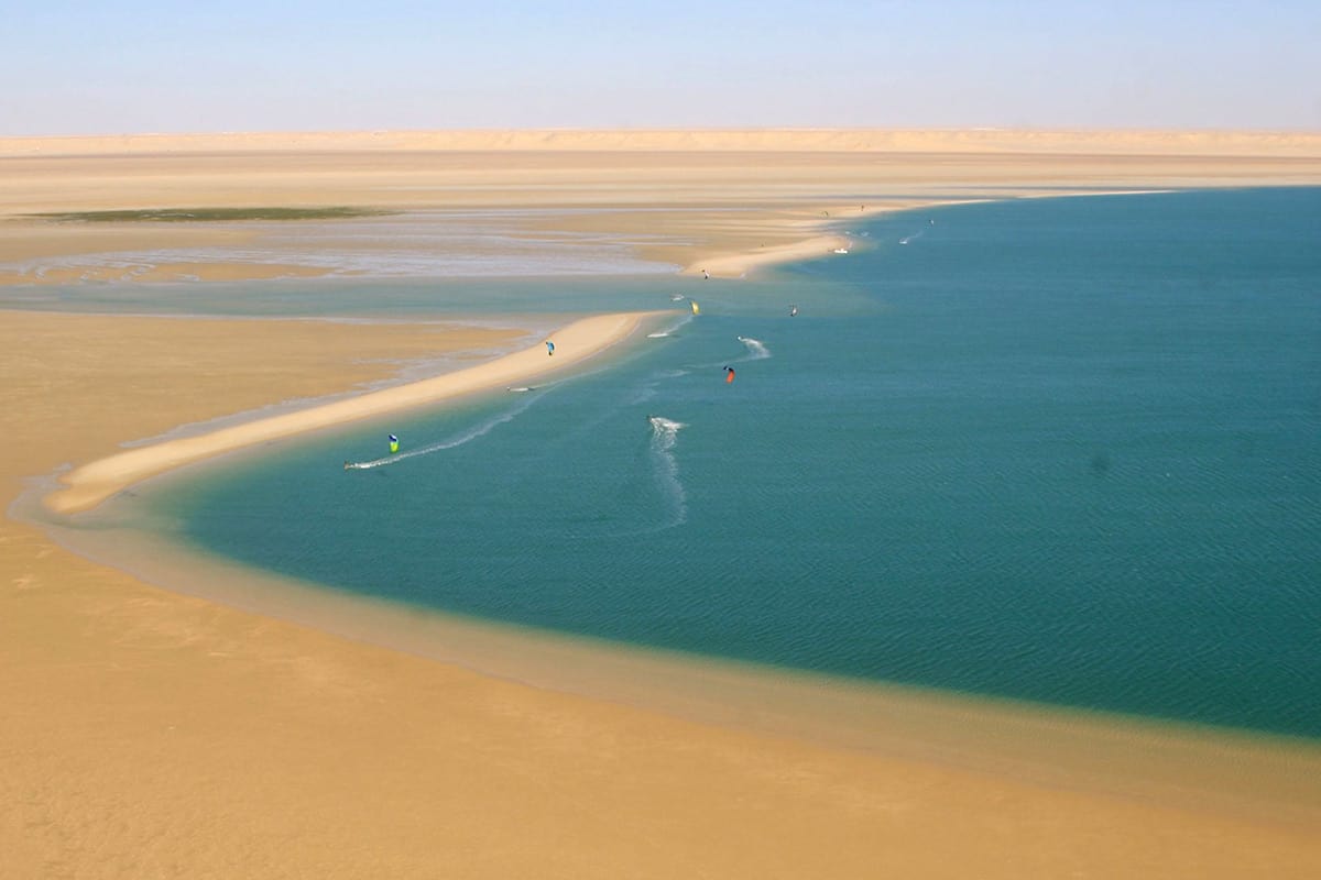 helder blauw water aan de rechterkant ontmoet het gouden zand van dakhla's woestijn aan de linkerkant. we kunnen nauwelijks een stuk of 5 kitesurfers op het water zien.