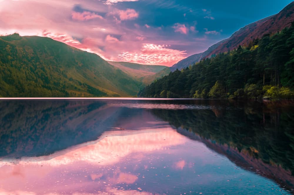 pink sunset over the mountains, forest, and upper lake of glendalough, ireland.