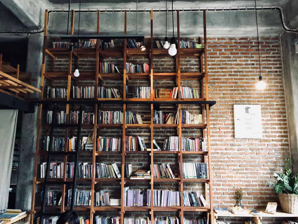 een boekenplank van vloer tot plafond tegen een bakstenen muur in een hip café in chiang mai, thailand