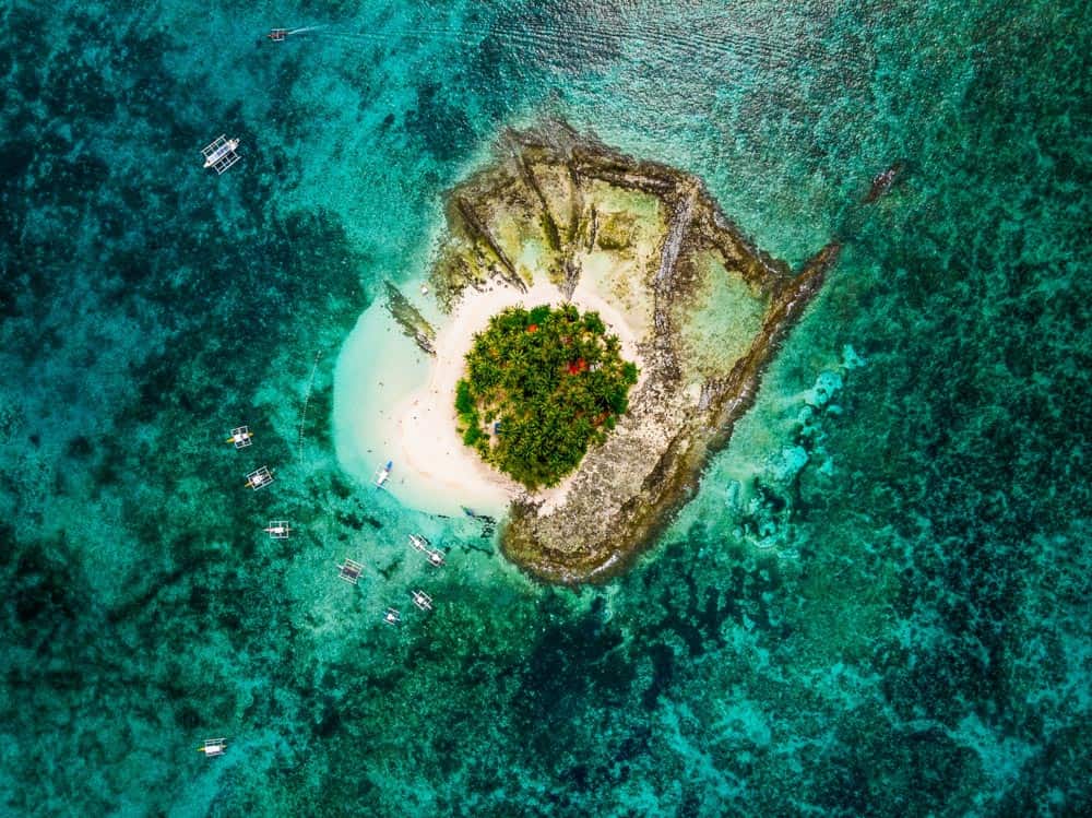 aerial view of guyam island off the coast of siargao island, philippines. the tiny island is a diving location, surrounded by turquoise water and coral reef.