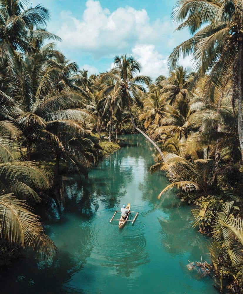 Ein Fischerfloß schwimmt auf einem türkisfarbenen Fluss, umgeben von Palmen auf der Insel Siargao, Philippinen