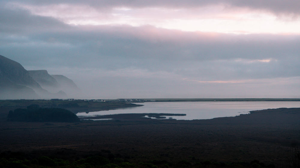 sunset landscape on achill island. keel lake is reflecting the pink-ish sky, and there are some misty sea cliffs to the left.