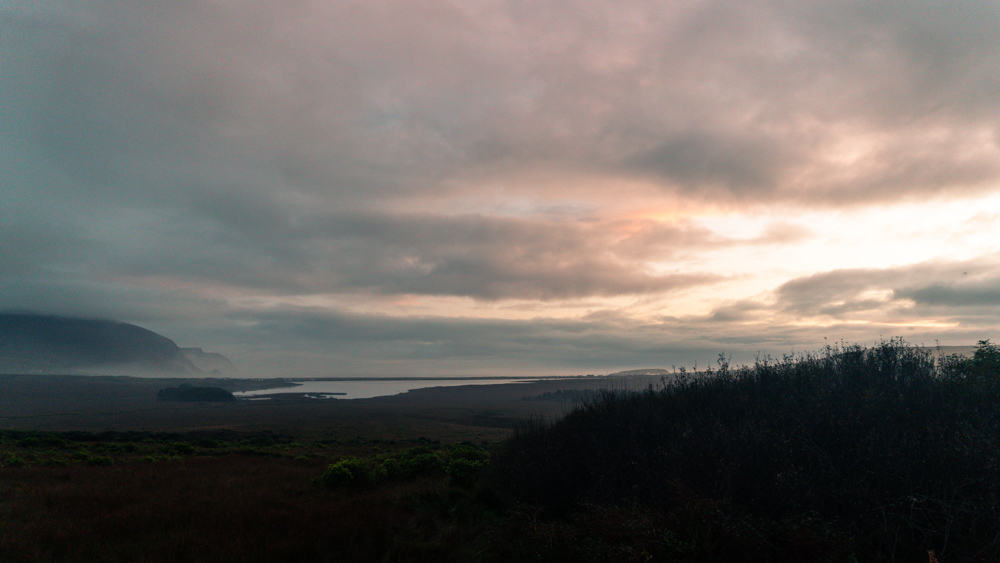 paysage de coucher de soleil sur l'île d'achill. le lac keel reflète le ciel rosé, et il y a quelques falaises de mer brumeuses à gauche.