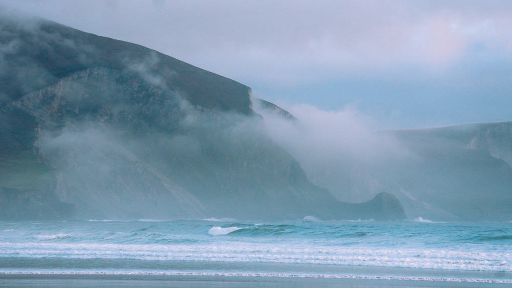 les falaises brumeuses de la plage de keel, sur l'île d'achill, dans le comté de mayo (irlande). les vagues déferlent au pied des falaises.