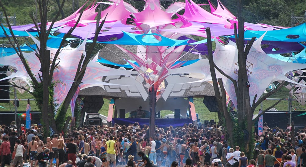 Plan de la foule du festival Ozora sur une scène de musique avec des décorations psychédéliques au-dessus de la tête.