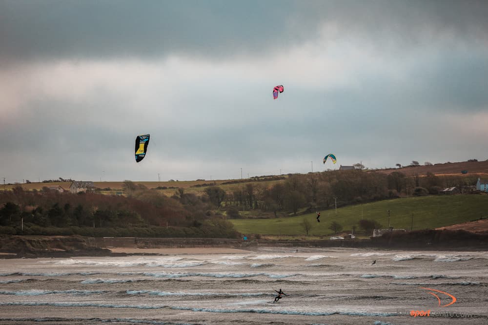 a moody cloudy day at the kitesurfing beach in ireland. three kites fly in the air.