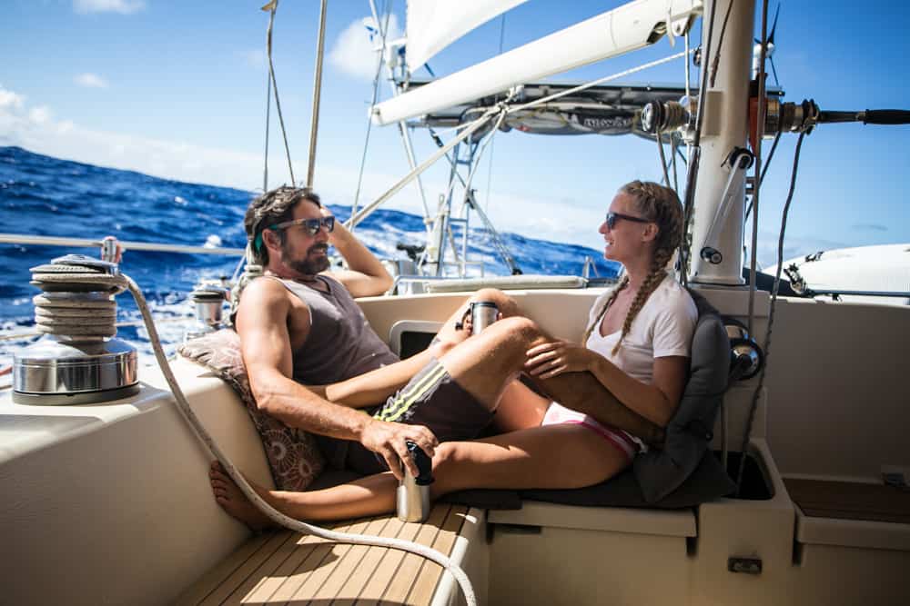 Brian and Karin sitting onboard SV Delos, cruising through the ocean on a sunny day