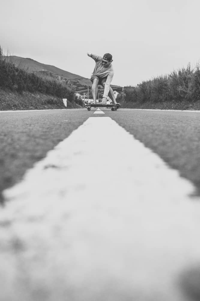 Brian Trautman of SV Delos skateboarding. He's grabbing the board + skating down the middle of a tramacked road. The photo is in black and white.