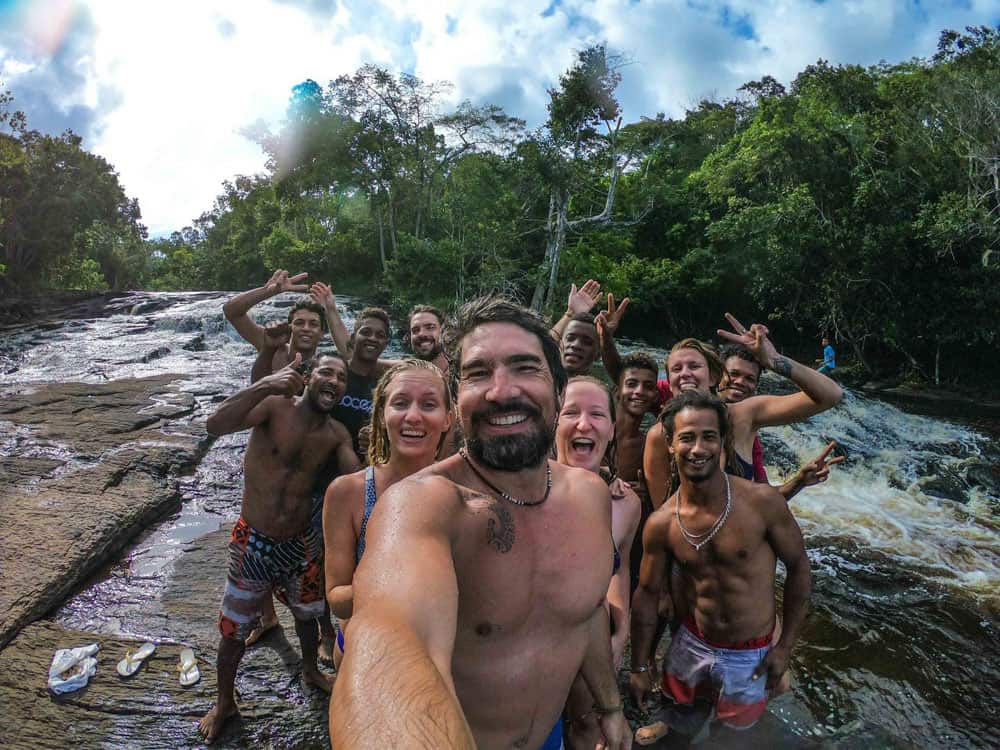 De SV Delos bemanning staat naast een groep lokale bewoners in Brazilië. Ze zijn bij een rivier ergens afgelegen, iedereen lacht en zwaait na wat plezier in het water.