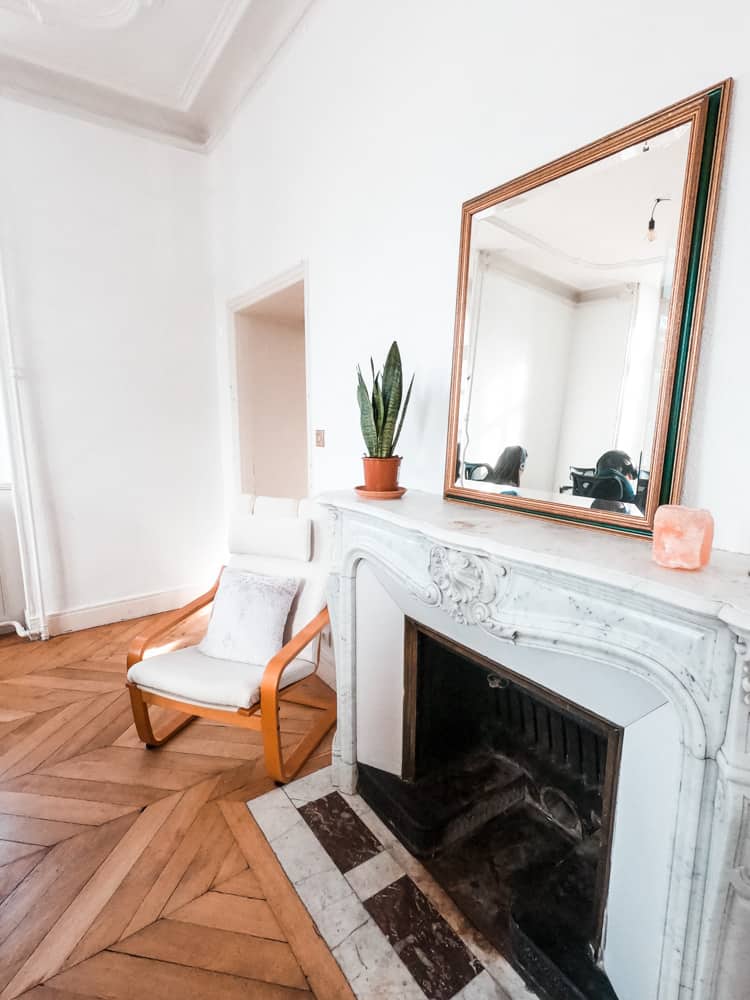 cheminée dans la salle de coworking de cloud citadel. il y a un miroir au-dessus, une chaise à côté et une plante sur la cheminée.