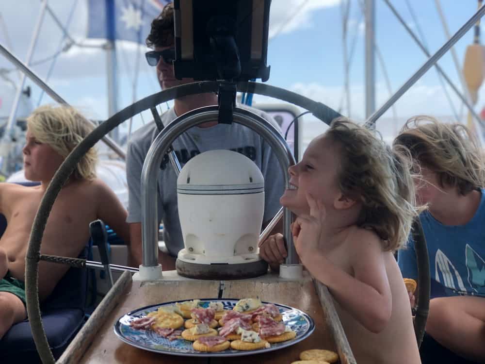 drei blonde Kinder entspannen auf einem Segelboot mit Papa am Steuer