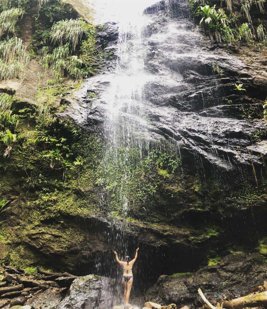 Erin im Bikini unter einem riesigen Wasserfall stehend, genießen Sie eine wilde Dusche.