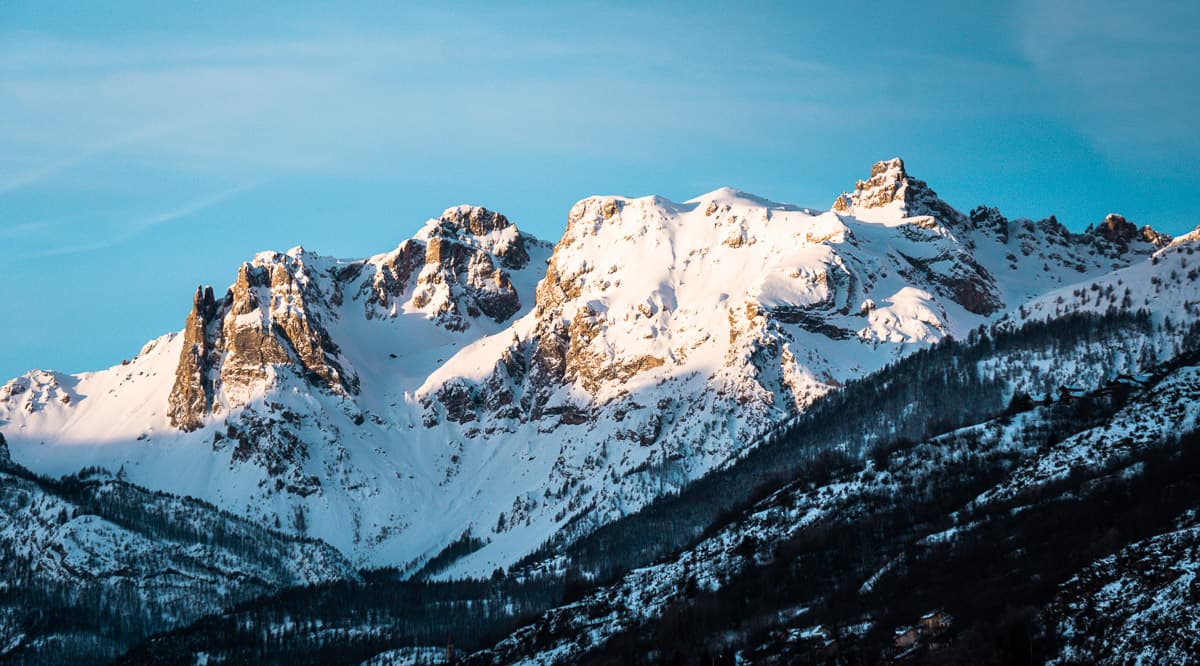 the snow covered mountains of serre chevalier, france. sunlight is hitting the highest peaks and a blue sky hangs overhead.