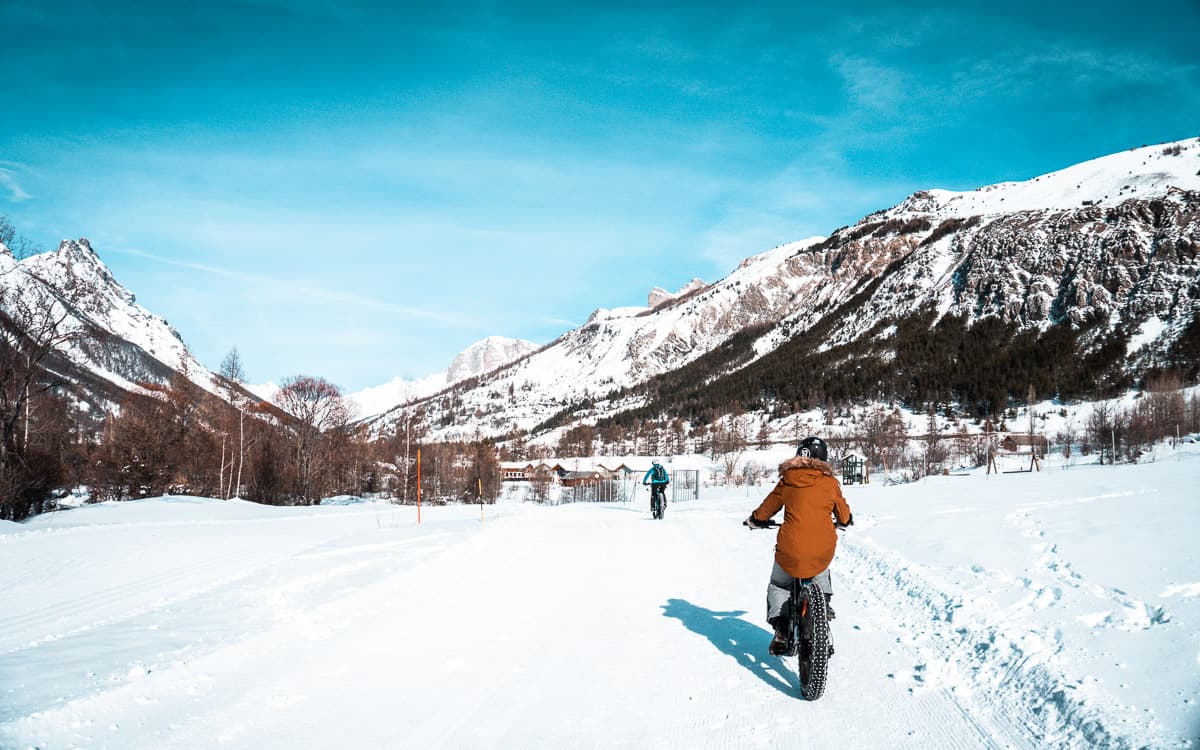 Grace fait du fat bike dans le parc national des Ecrins à Serre Chevalier. Il y a de la neige au sol, des montagnes en arrière-plan et un ciel bleu vif au-dessus de nos têtes.