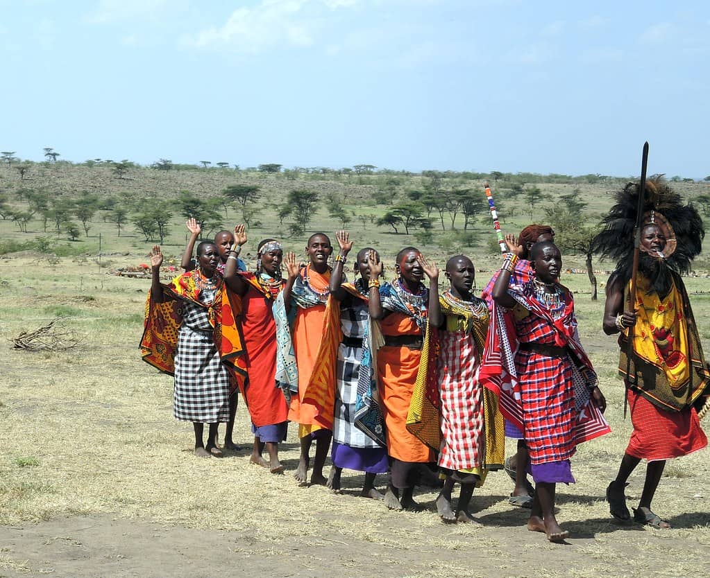 masai mara people wearing colourful robes and standing on parched dusty ground. 