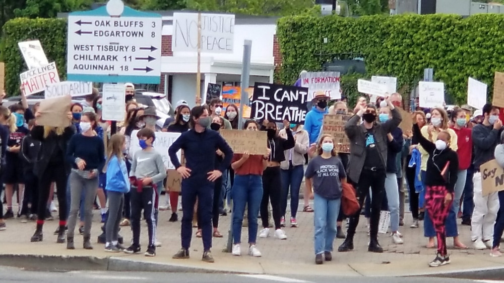 A crowd of people marching for the Black Lives Matter movement. There are several dozen people holding signs and everyone is wearing a face mask.